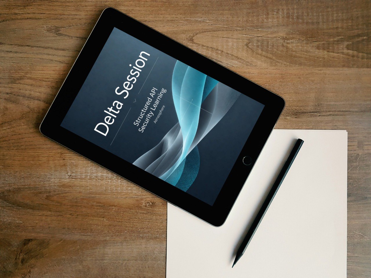 A black tablet lying on a wooden desk, angled diagonally, with a blank sheet of paper and a black stylus beside it. The tablet screen displays the text 'Delta Session' and 'Structural Analysis: Second Semester'.