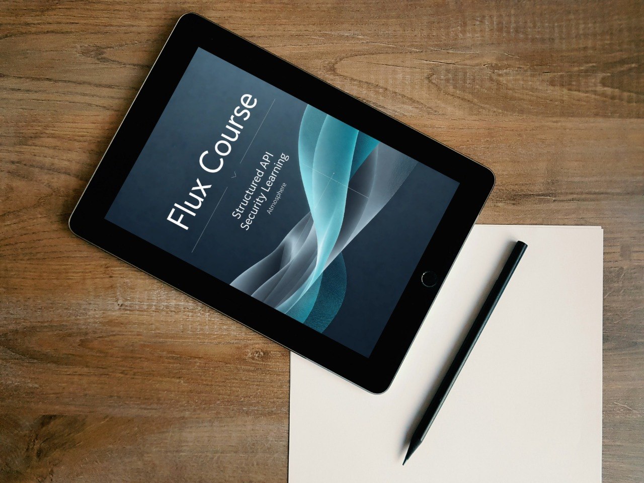 A tablet lying on a wooden desk, displaying a course cover titled 'Flux Course: Structured and Secure Learning.' A blank sheet of paper and a black stylus are placed beside it.