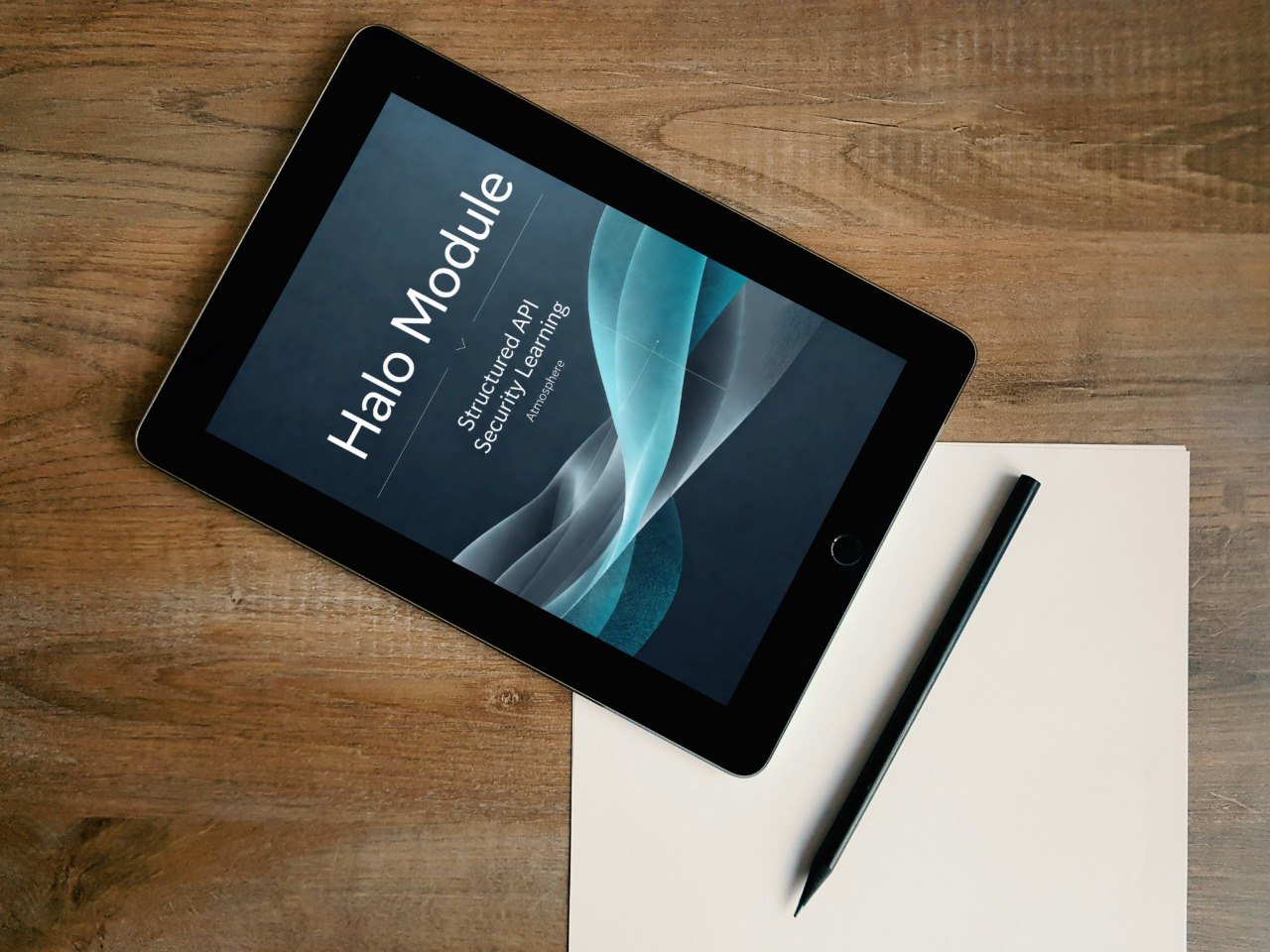 A tablet lying on a wooden desk, angled diagonally, with a blank sheet of paper and a stylus beside it. The tablet screen displays the text 'Halo Module' and 'Structured API Second Level'.