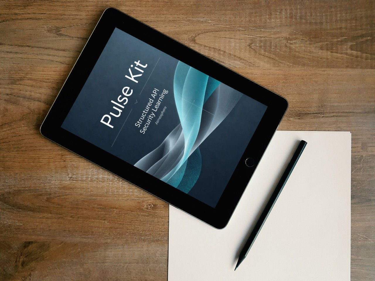 A tablet device lying on a wooden surface, displaying a cover titled 'Pulse Kit: Structured AI Second Language.' A blank sheet of paper and a black stylus are placed beside it.